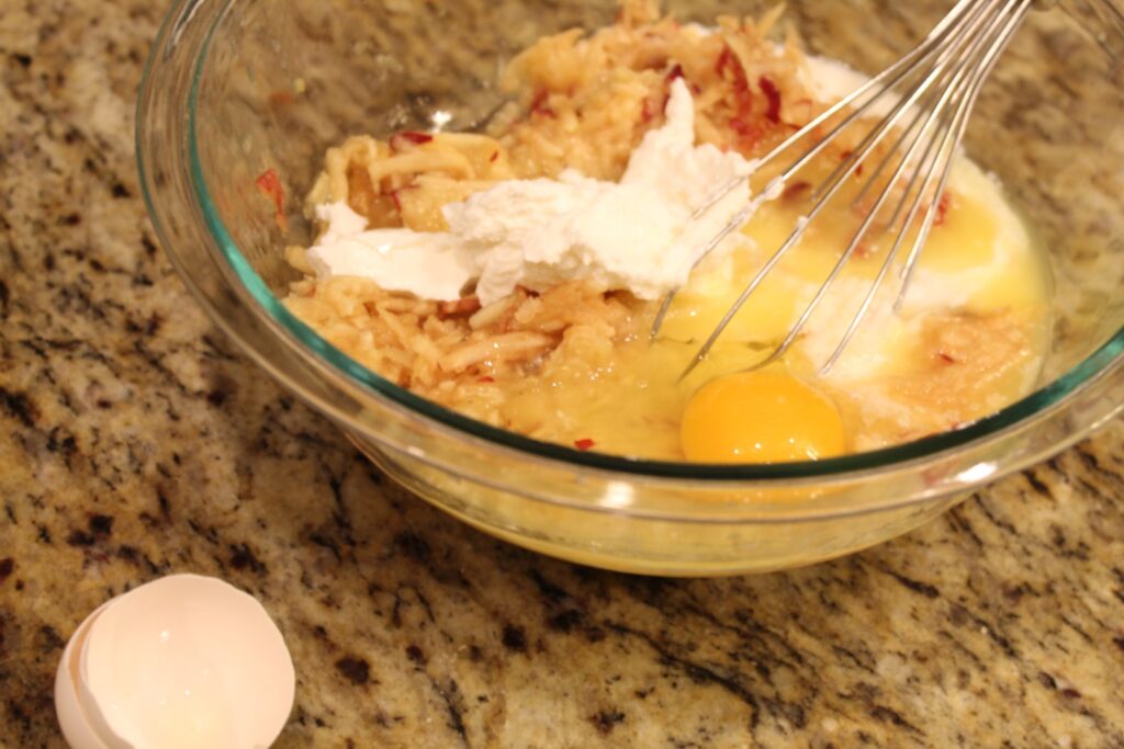 an unmixed bowl of ingredients including grated apple yogurt and an egg.