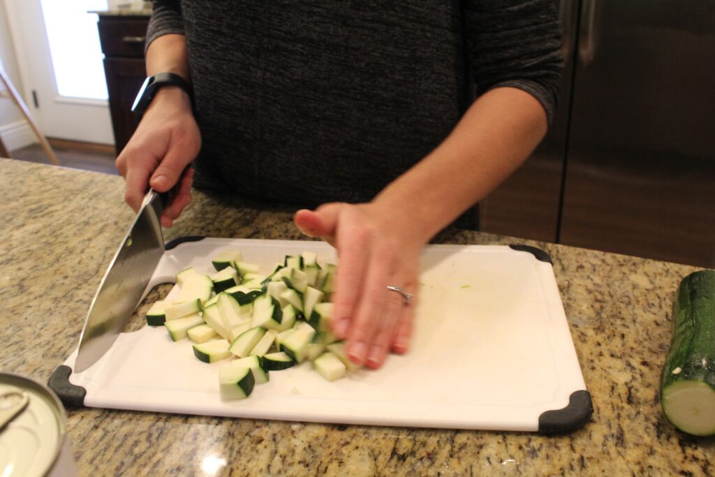 Someone dicing zucchini on a cutting board with a large knife.