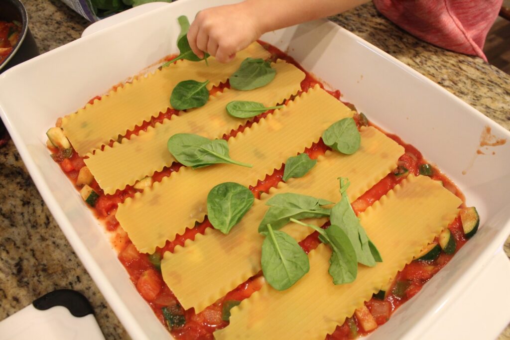 Adding spinach to a layer of veggie lovers lasagna.