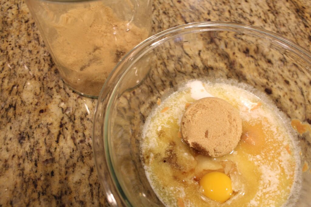 scoop of brown sugar on top of melted butter next to egg in a bowl.