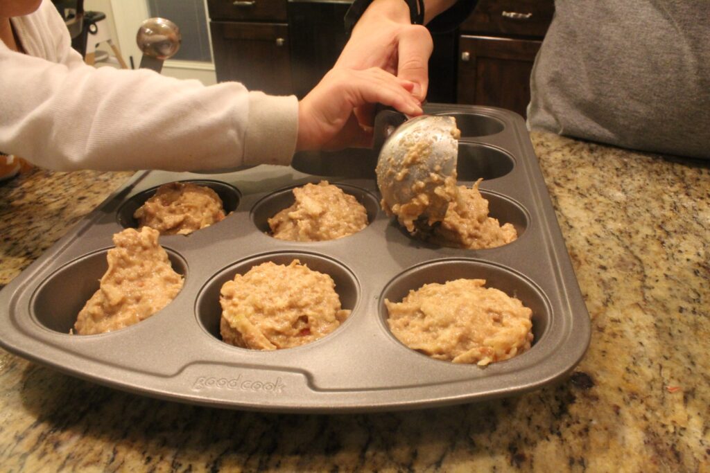 Using an ice cream scoop to put whole wheat apple banana muffin batter into a muffin tin.