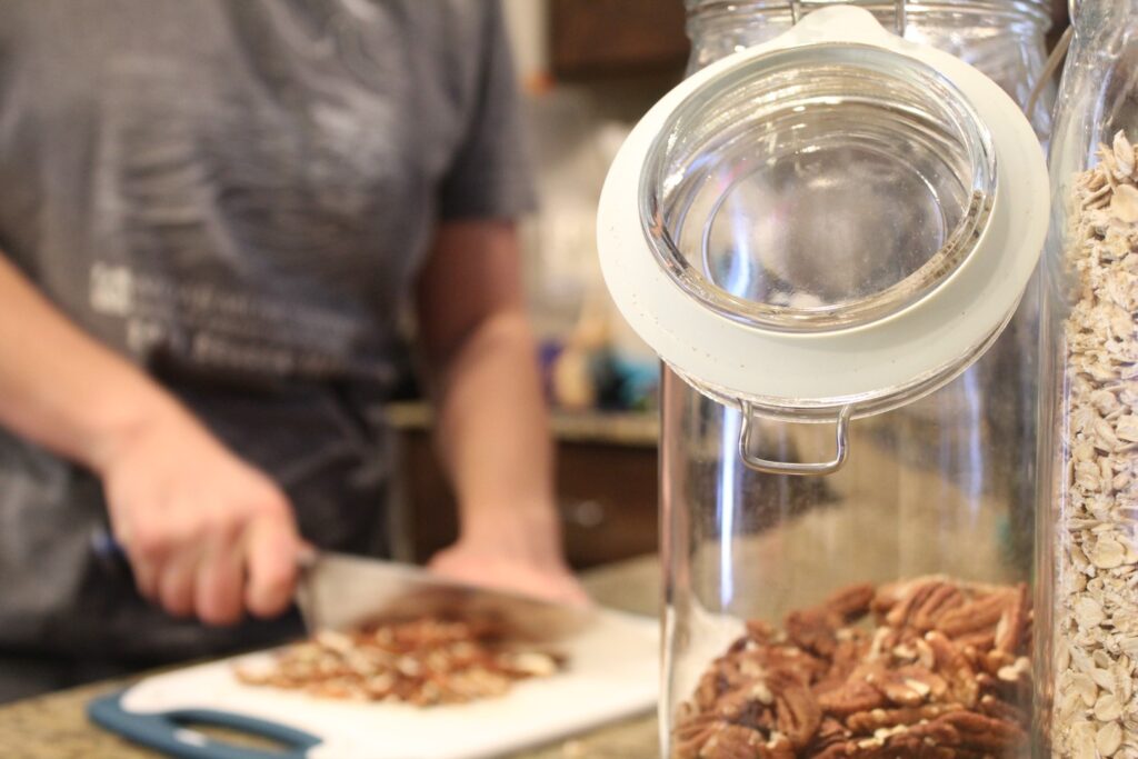 Close up of a jar of pecans with pecans being chopped in the background.