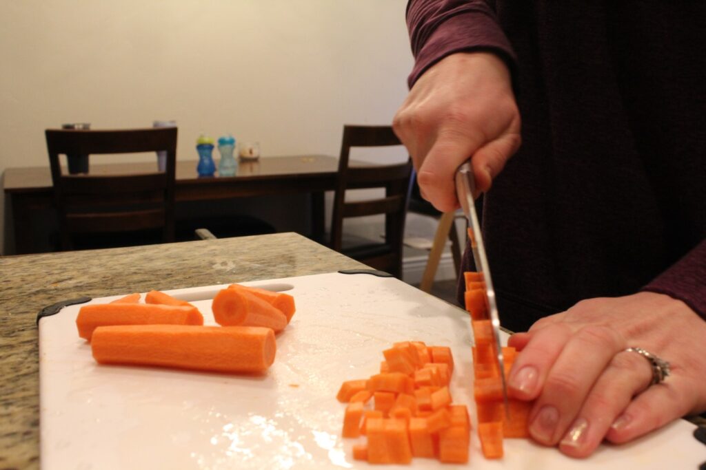 Finely dicing a carrot on a cutting board with a knife.