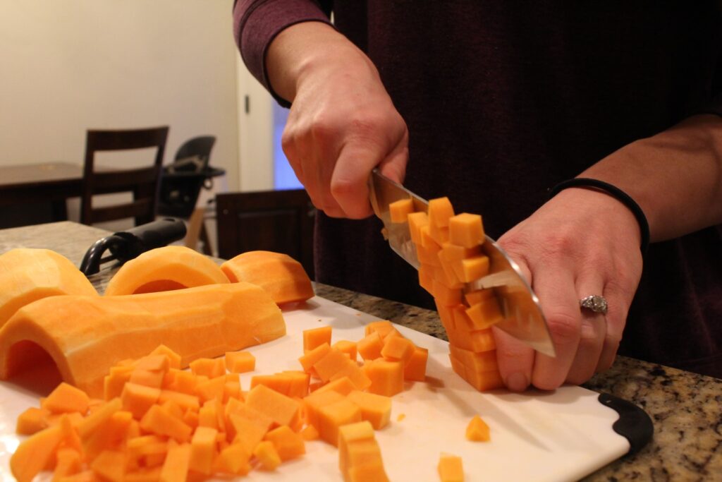 Dicing butter nut squash on a cutting board with a knife.