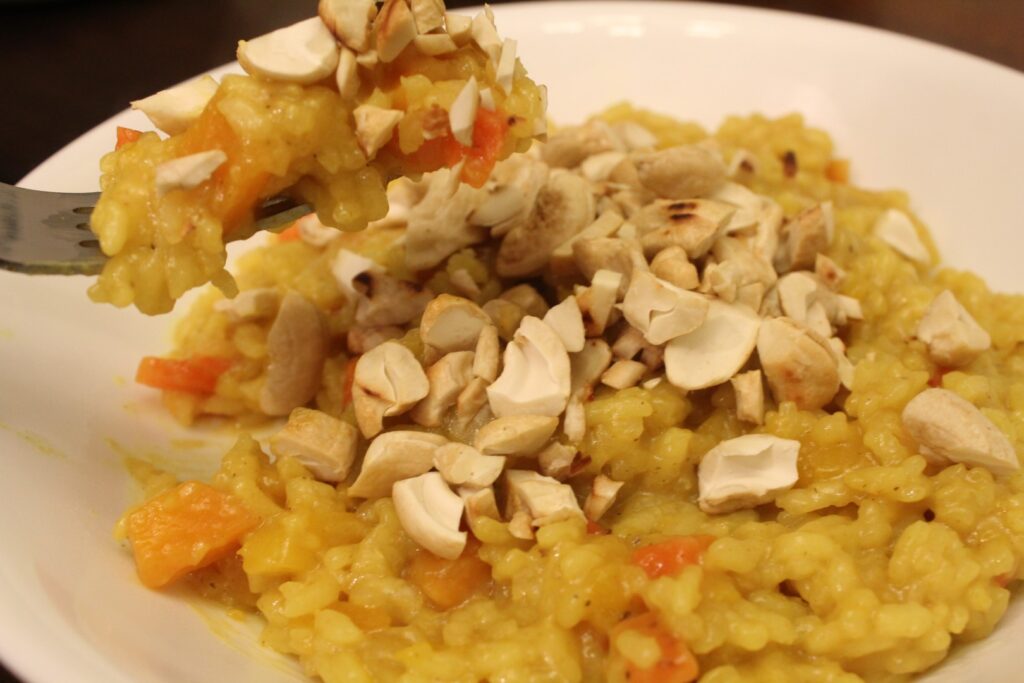 A fork of curried butternut squash risotto, over a bowl, topped with cashews.