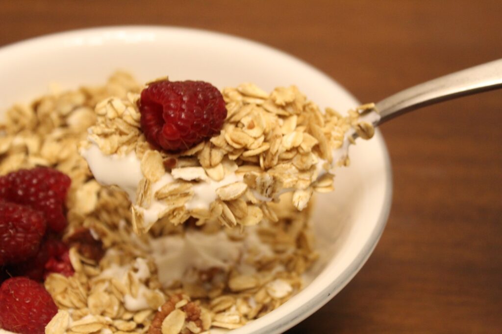 Granola and yogurt on a spoon topped with a raspberry.