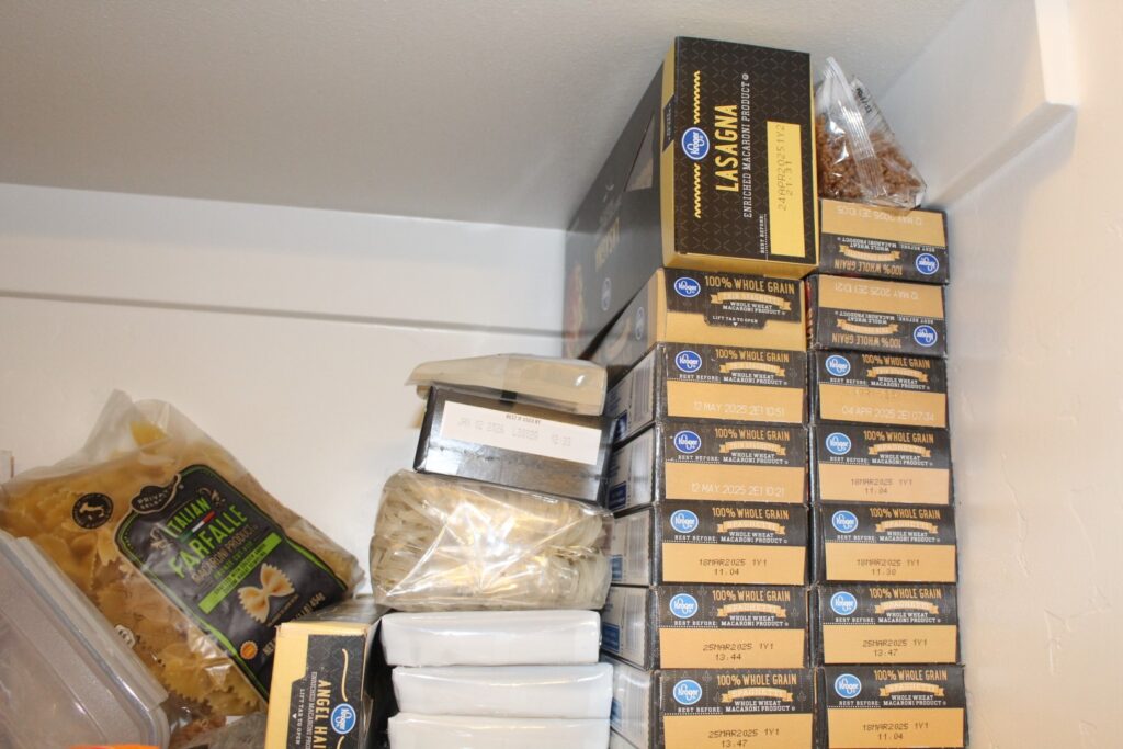 A stack of spaghetti boxes, and a pile of noodles and pastas in a pantry.