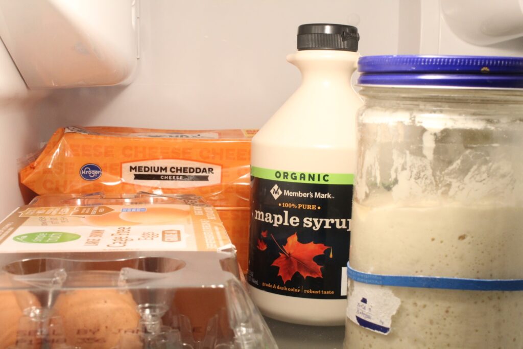 Eggs, cheese, maple syrup, and sourdough starter in a fridge.