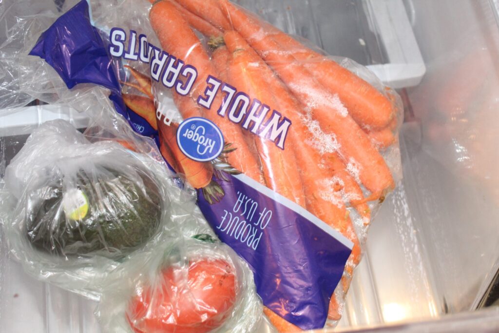 Refrigerator drawer with carrots a tomato and an avocado.