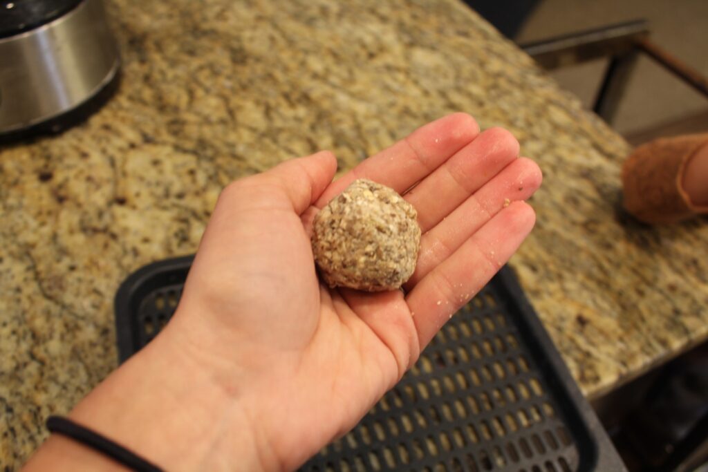 A hand with an uncooked mushroom meatball.