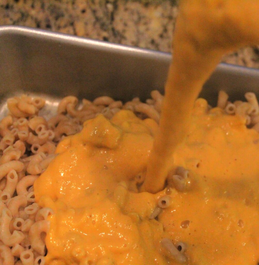 Sweet potato macaroni sauce being poured over noodles.