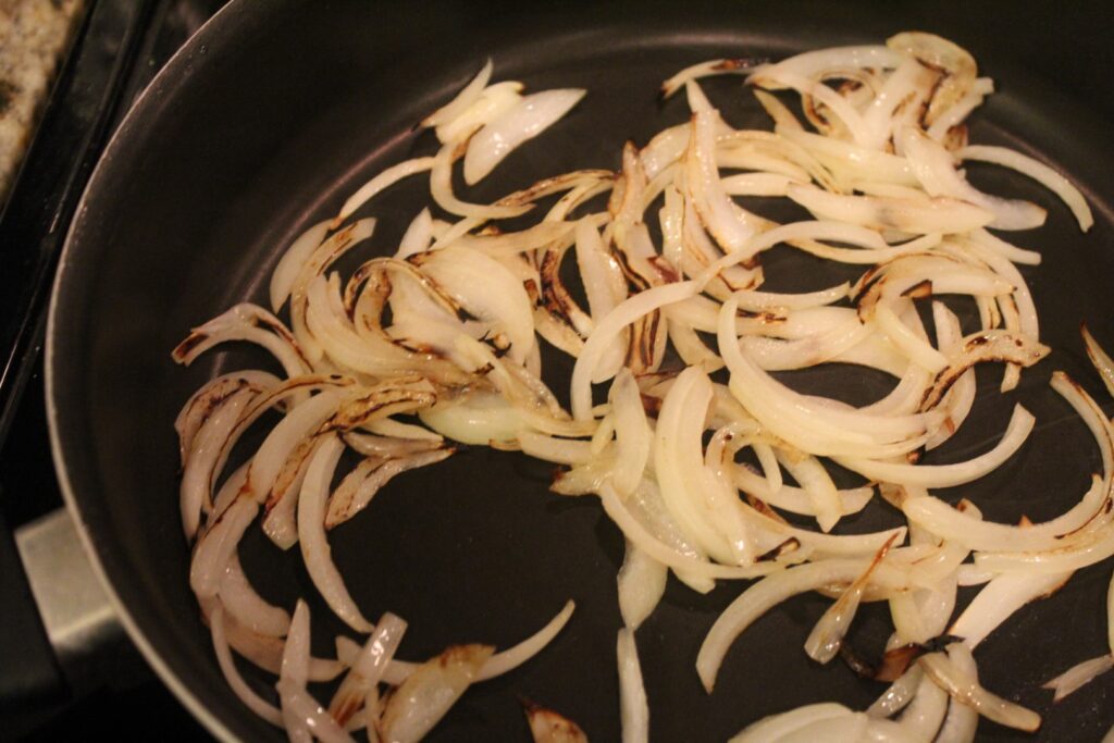 Slivered onions cooking in a frying pan.