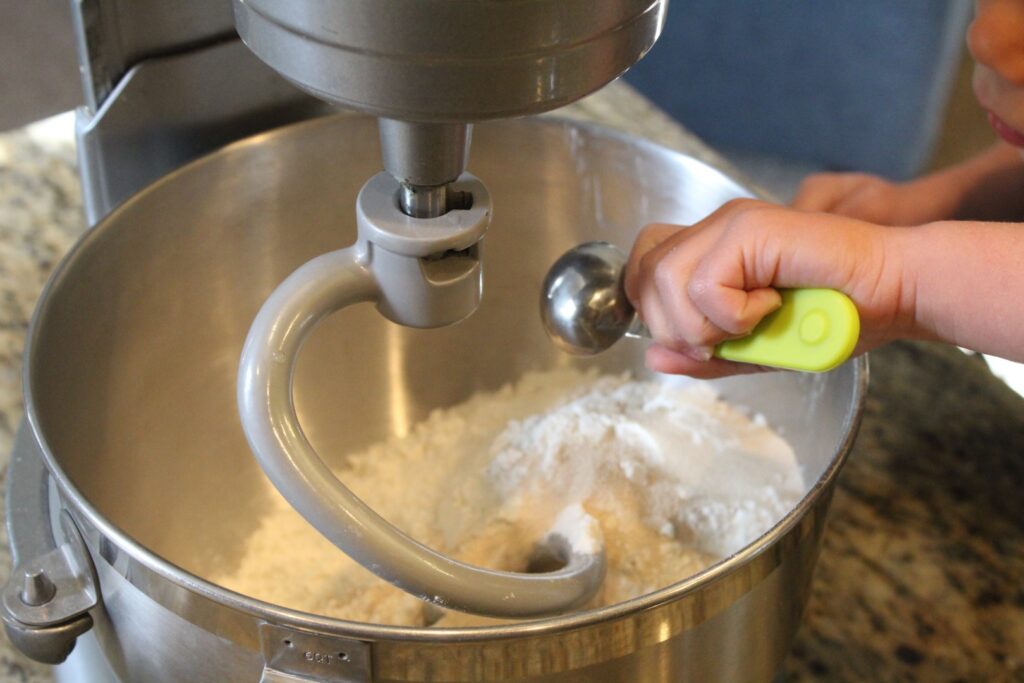 A small hand pouring a teaspoon full of yeast into a stand mixer.