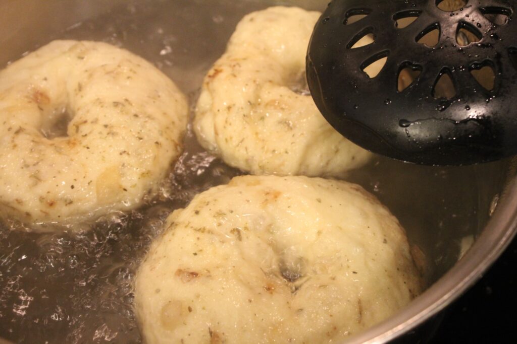 Boiling onion bagels in a large pot.