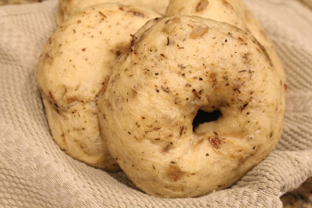 Onion bagels in a bowl lined with a towel.