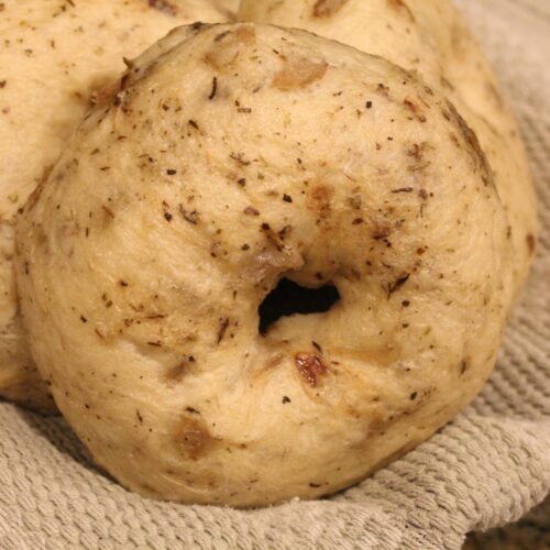 close up of homemade onion bagels in a towel lined bowl.