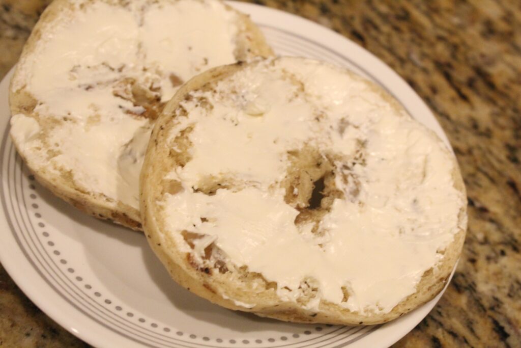 a bagel on a plate sliced in half covered in cream cheese.