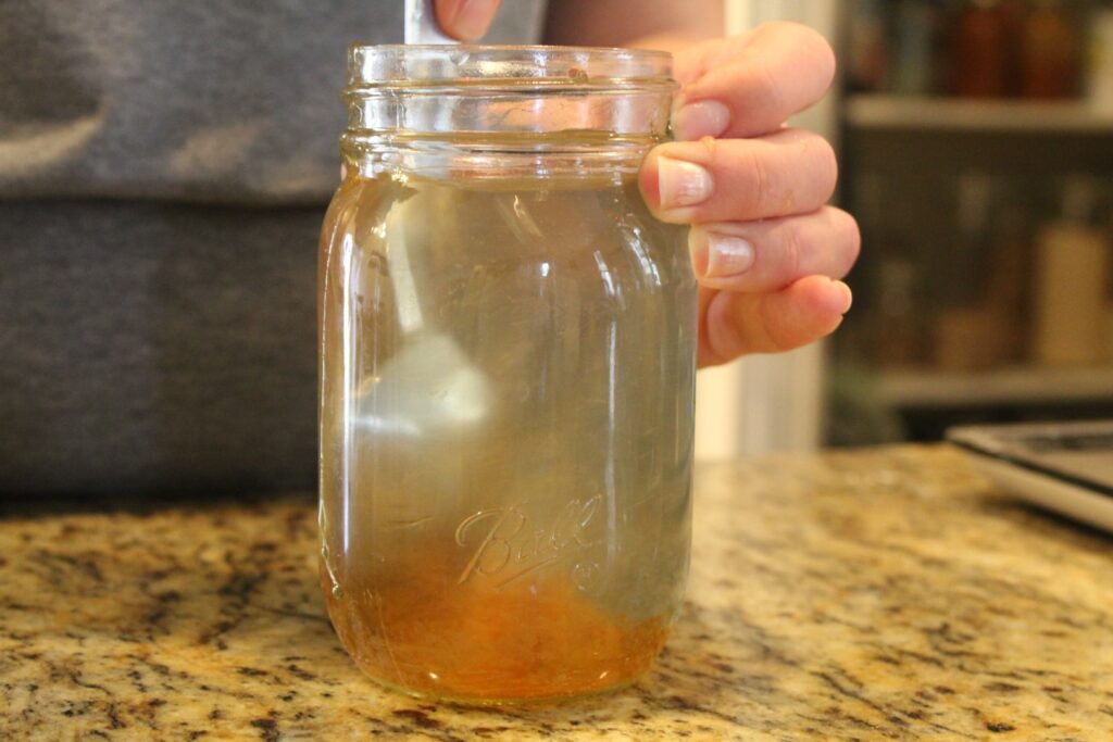 Stirring honey into water in a glass jar.