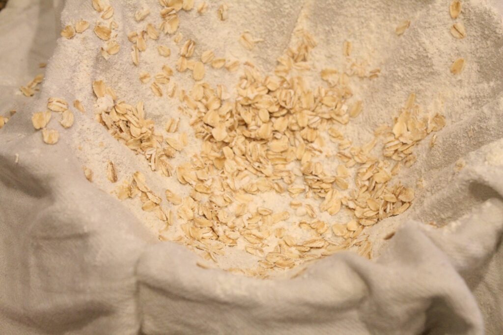 A cloth covering a bowl dusted with oats and flour.