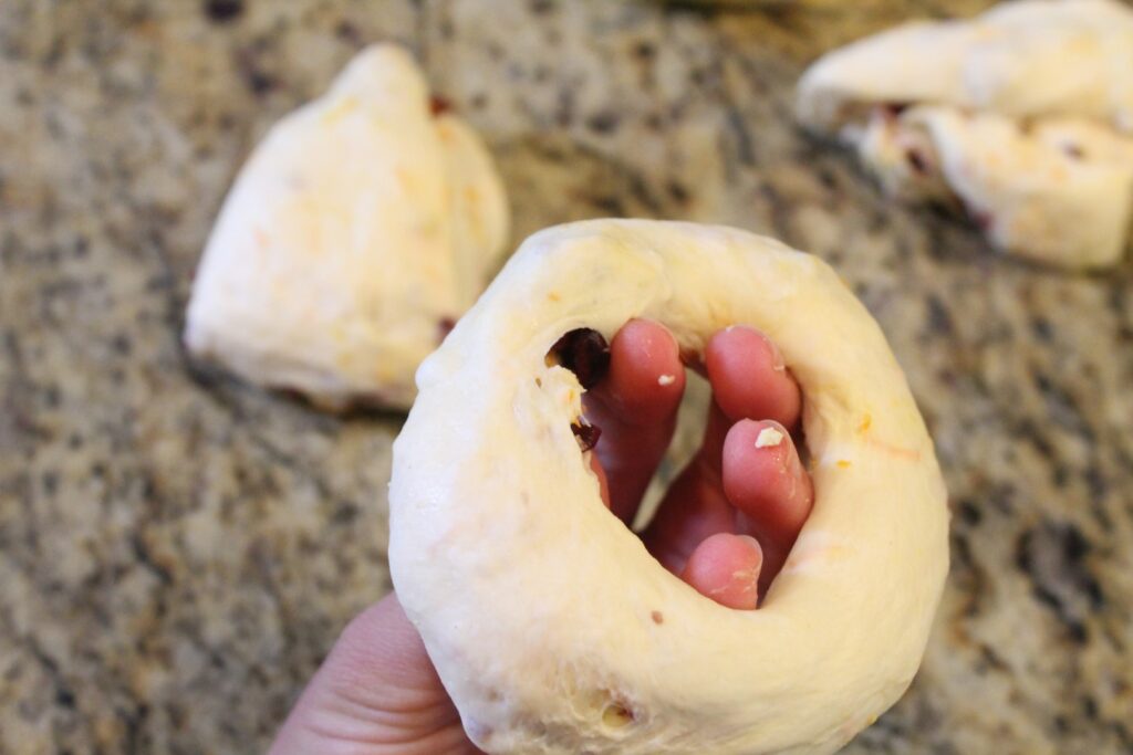 Fingers stretching out the hole in the center of a bagel's dough.