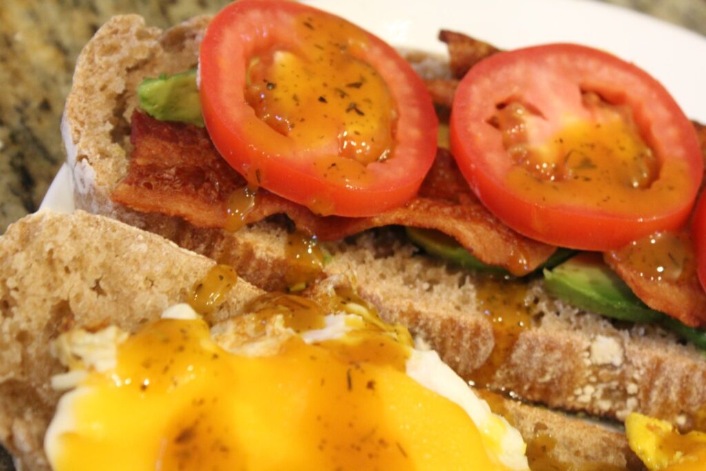 Honey mustard vinaigrette topping a sandwich with bacon eggs and vegetables.