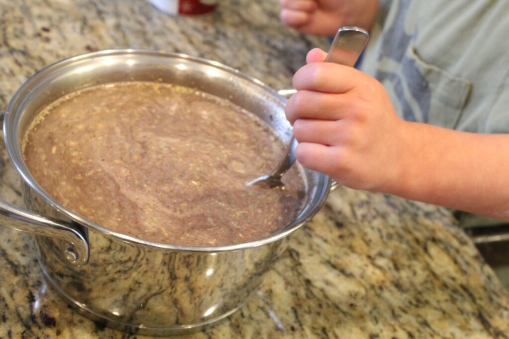 a small hand mixing seasonings into a pot of water and lentils with a spoon.