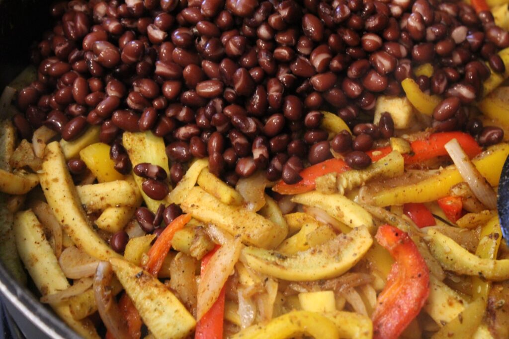 Adding black beans to a pan with fajita vegetables. 