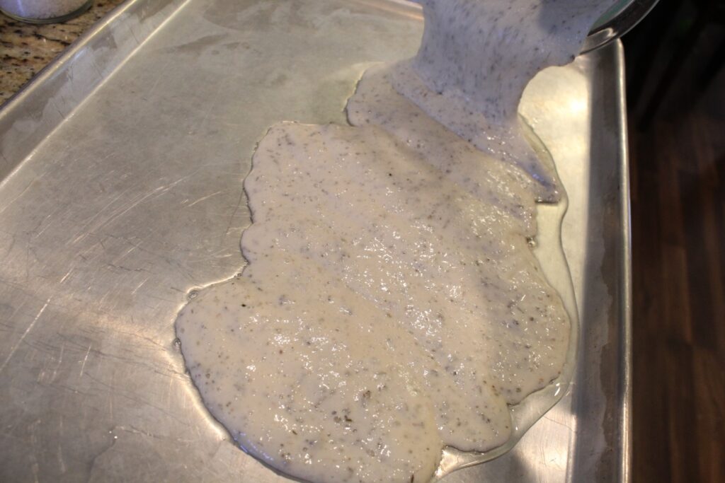 Pouring sourdough cracker batter onto a pan with olive oil