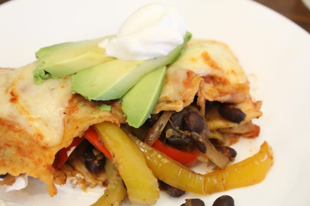 black bean fajita enchilada topped with avocado and sour cream.