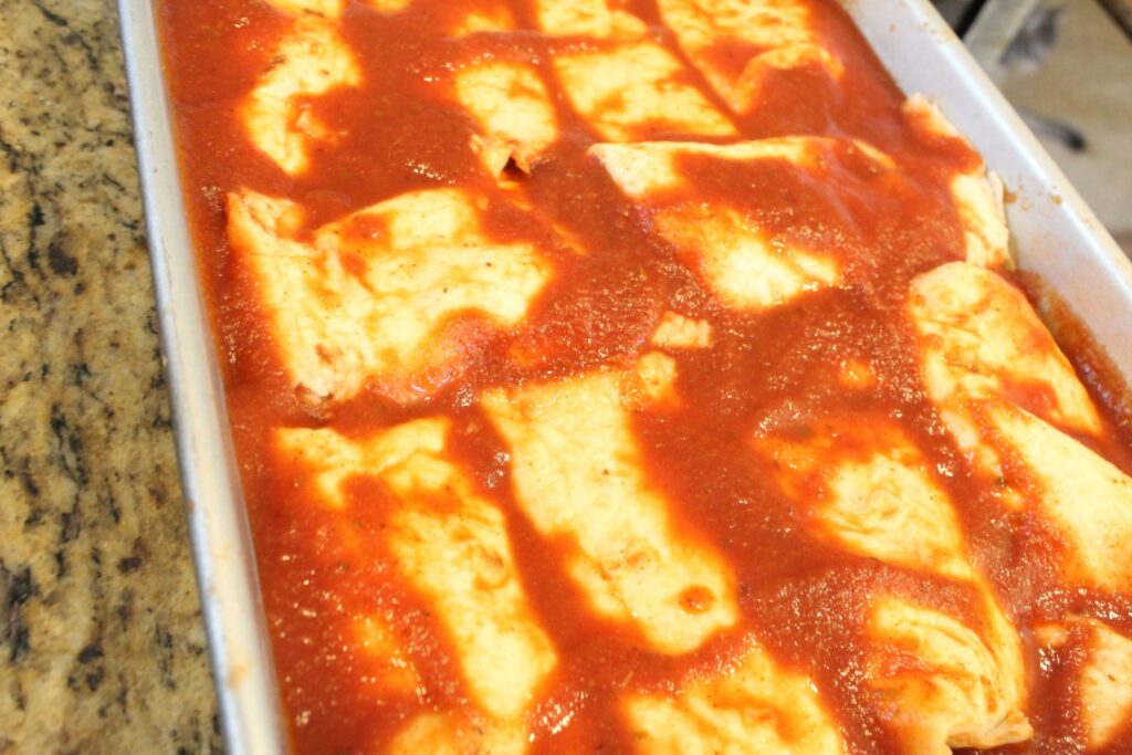 9x13 pan filled with Enchiladas covered in red sauce.