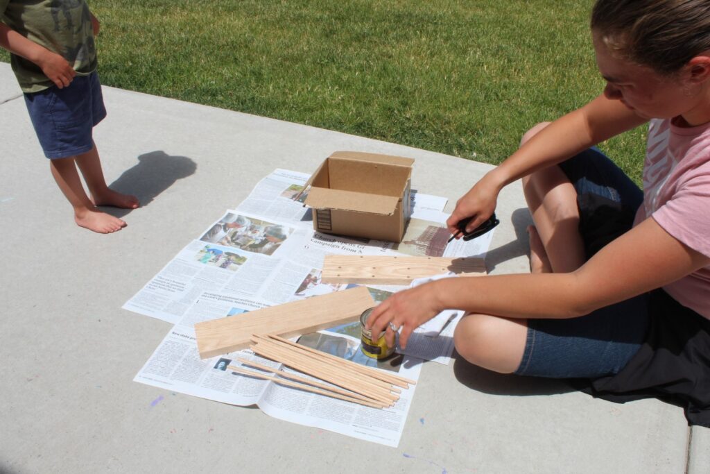 woman setting out supplies on news paper to stain wood.