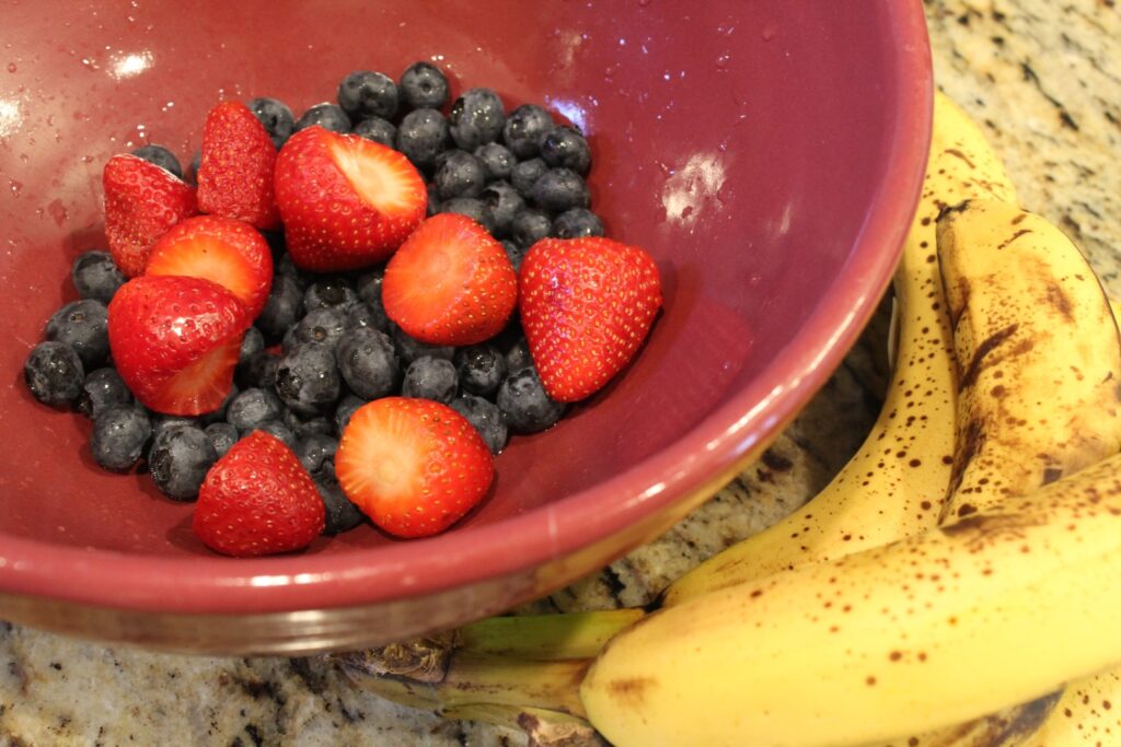 a bunch of bananas next to a bowl of strawberries and blue berries.