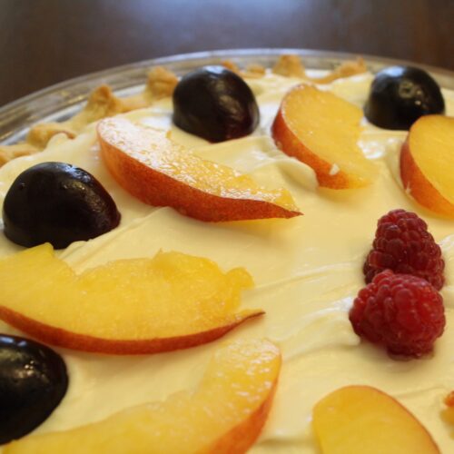 a cream cheese pie topped with peaches, raspberries, and cherries