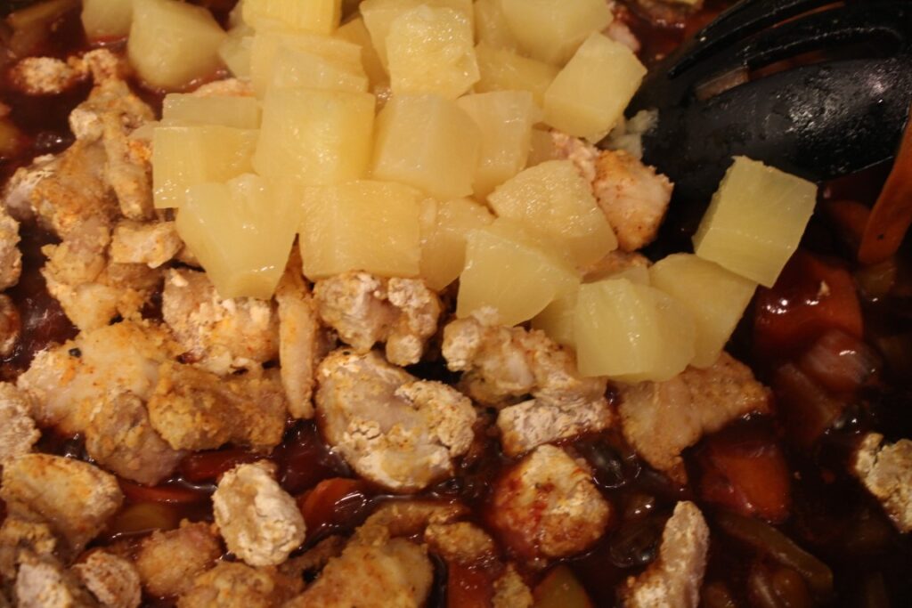 Adding chicken and pineapple to sweet and sour sauce. 