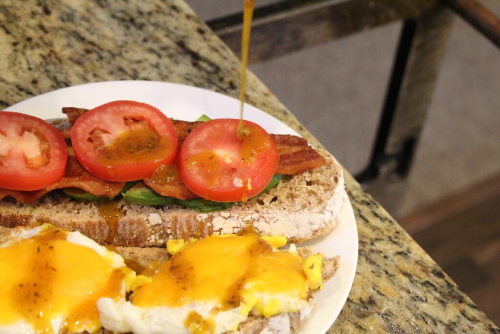 Vegetable topped breakfast sandwich being drizzled with honey mustard.