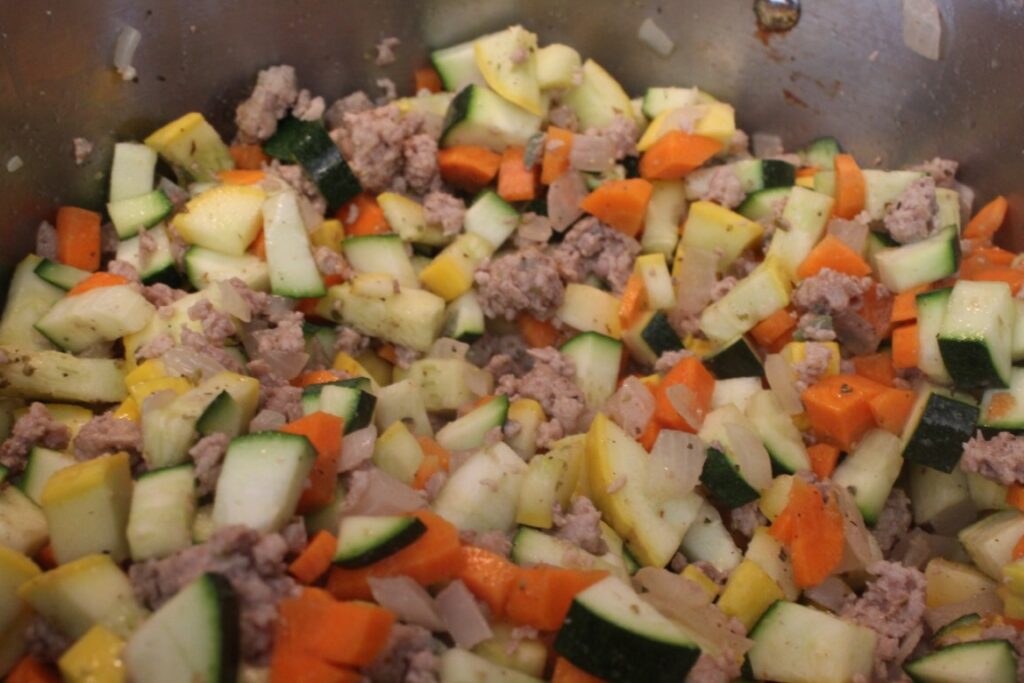 Cooking diced carrots onions and summer squash with ground pork sausage.