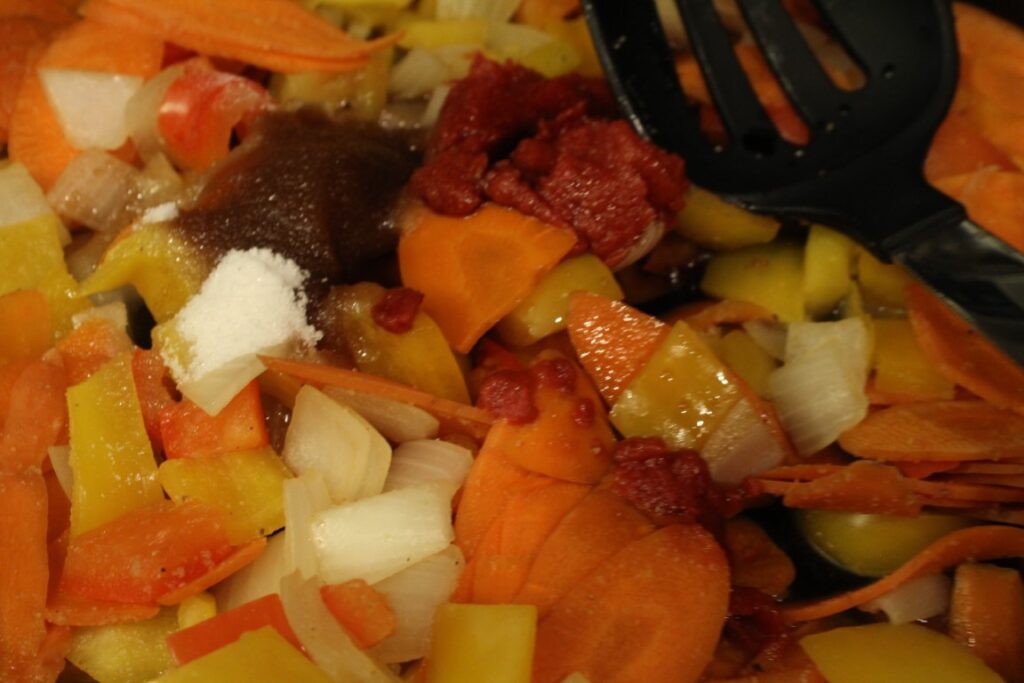 Adding sauce ingredients to a pan of sauteed vegetables.