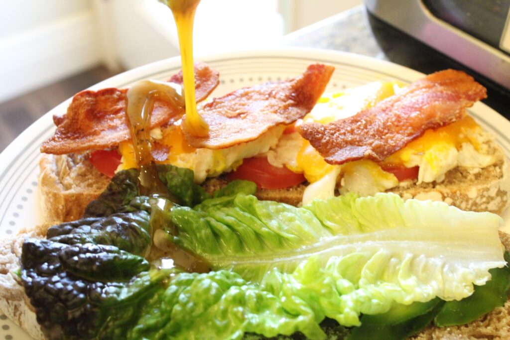 Breakfast sandwich with lettuce and tomatoes being drizzled with honey mustard. 