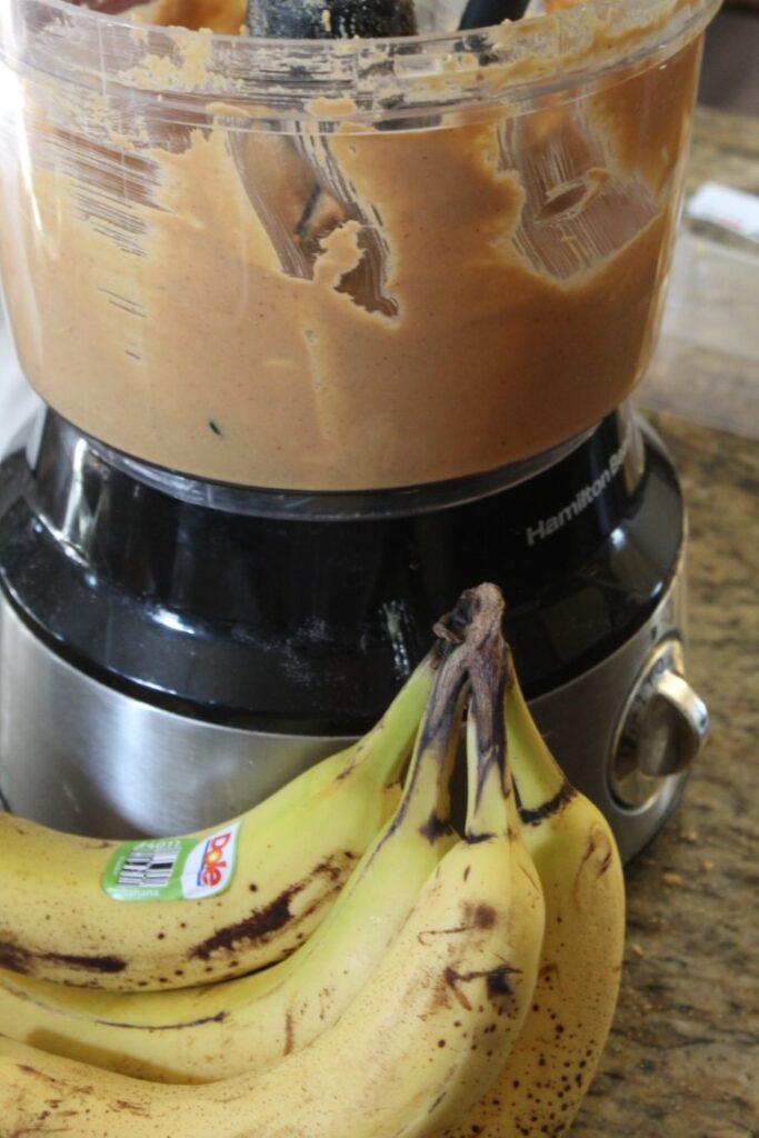 a bunch of bananas placed by homemade peanut butter in a food processor.