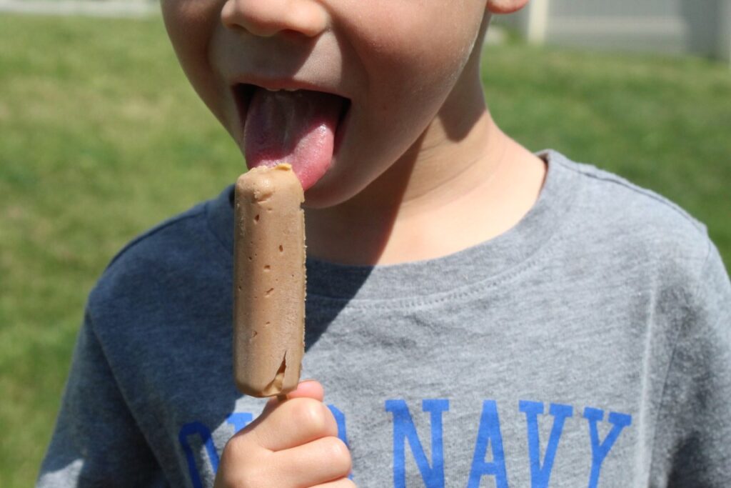 Young boy licking a 2 ingredient peanut butter banana Popsicle. 