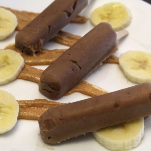 Peanut butter banana popsicles on a plate spread with peanut butter and bananas