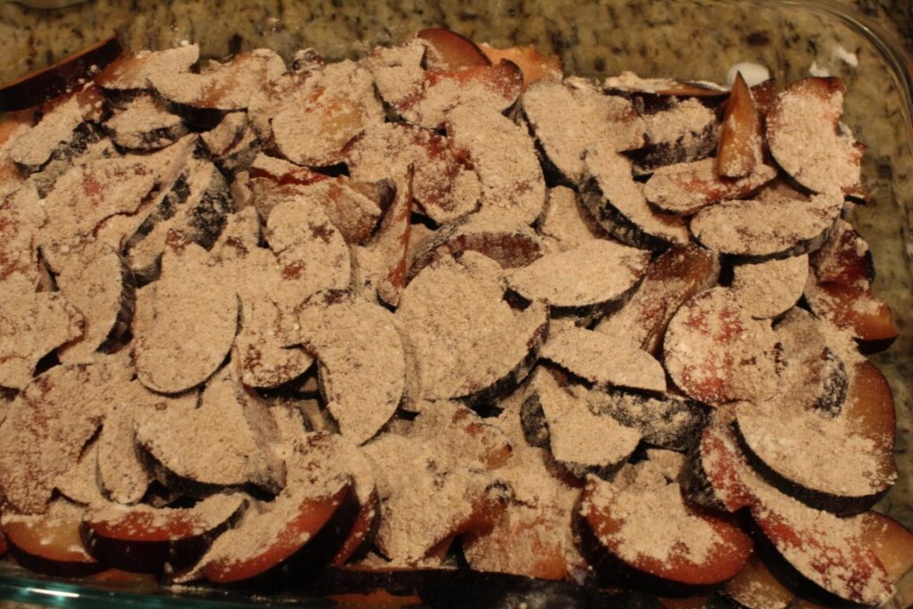 Sliced plums in a 9x13 pan sprinkled with flour sugar and seasonings. 