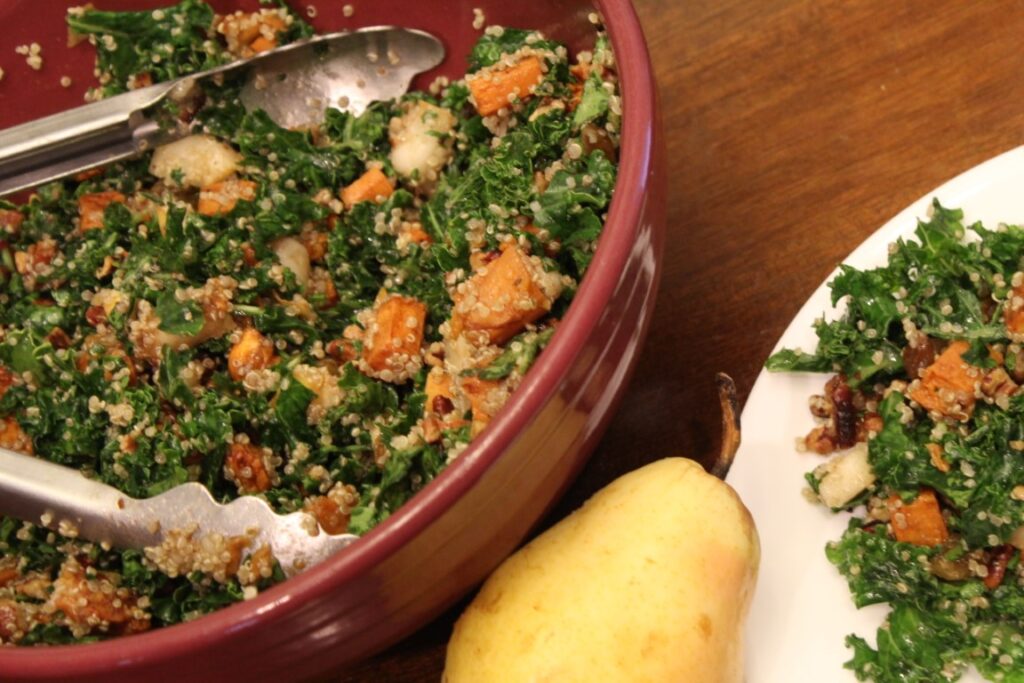 A pear with a plate and bowl of fall kale salad.