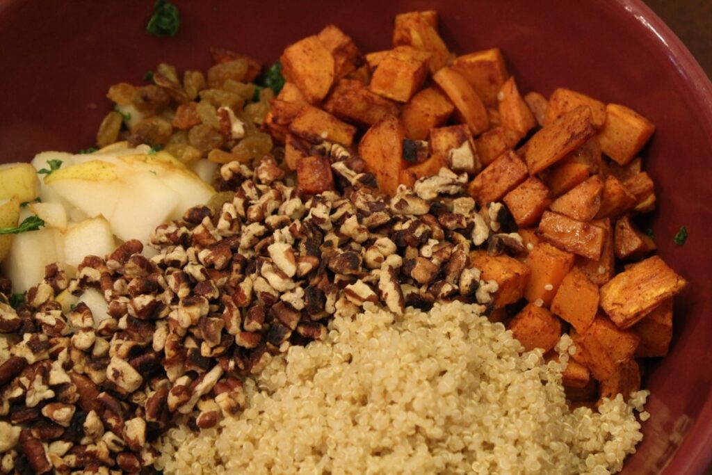 Bowl of salads topped with roasted sweet potato, raisins, quinoa, walnuts, and pear.