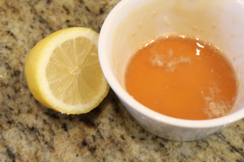 Half a lemon beside a bowl with lemon juice and honey.