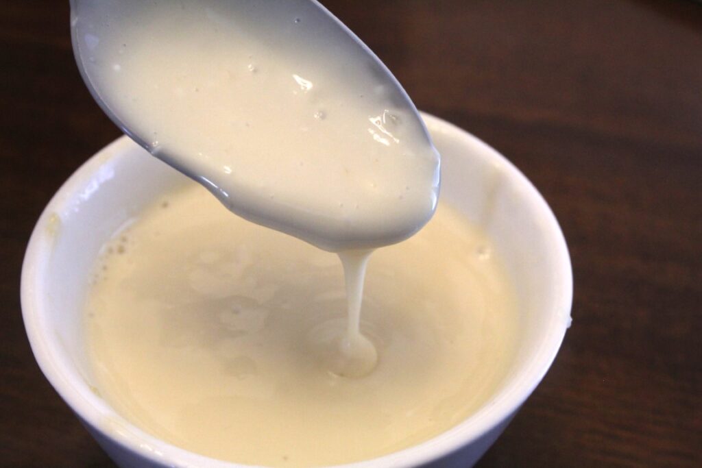 Spoon of lemon yogurt dressing dripping into a bowl.