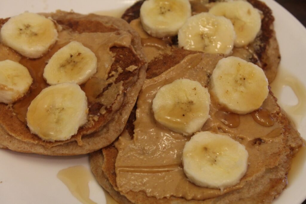 whole wheat banana pancakes topped with peanut butter, banana slices and maple syrup.