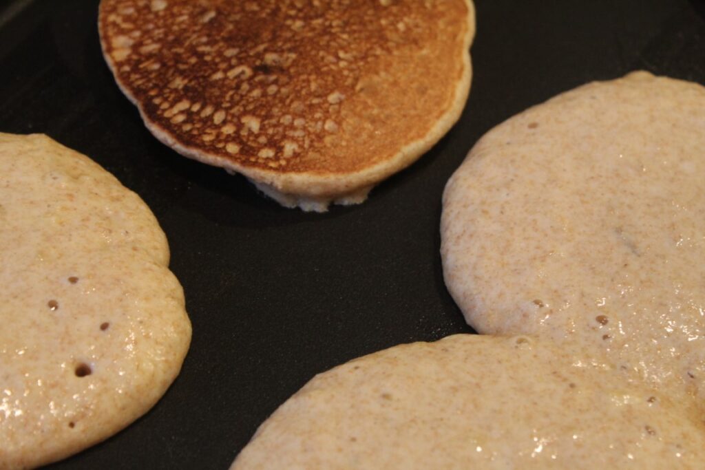 Whole wheat banana pancakes cooking on a griddle.