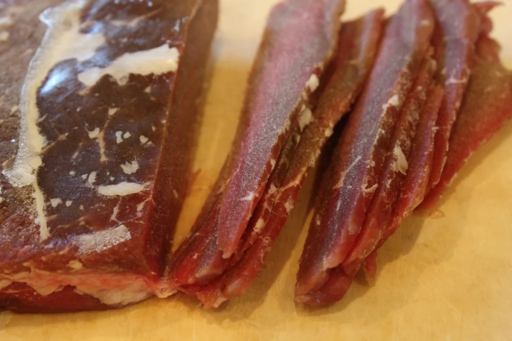 frozen raw beef being thinly sliced.