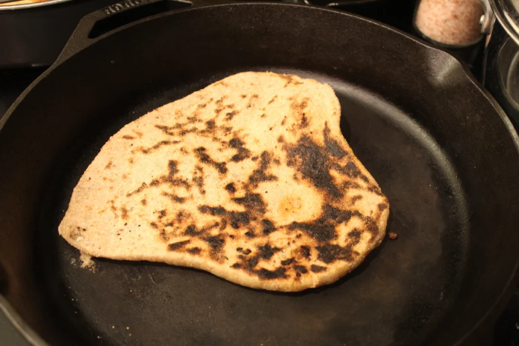 piece of sourdough sweet naan cooking in a cast-iron skillet.